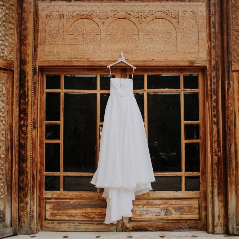 Robe de mariée suspendue devant une porte en bois sculpté marocaine